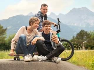 Junge Frau und zwei Jugendliche sitzen am Boden beim Pumptrack in Schattdorf und schauen aufs Handy.